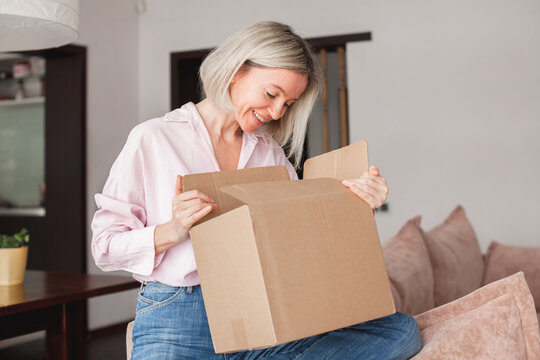 woman sitting on couch at home opening carton box received parcel package
