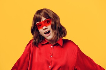 an attractive, stylish woman stands on a yellow background in a red shirt and glasses of an interesting shape, smiling happily. Horizontal photo with empty space