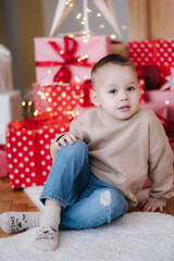 Portrait of cute little boy at home during winter holiday. Christmas tree and lot of presents