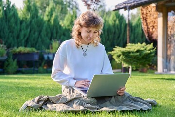 Teenage girl sitting on the grass using a laptop