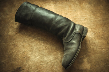 A long leather boot on a wooden background.An old boot is lying on the floor. Repair of old shoes. Fix the shoes.