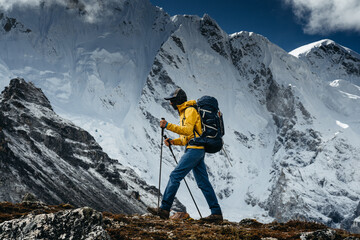 Brave tourist climb on altitude cloudy mountains. Solo traveler wearing professional backpack standing in front of high mountain