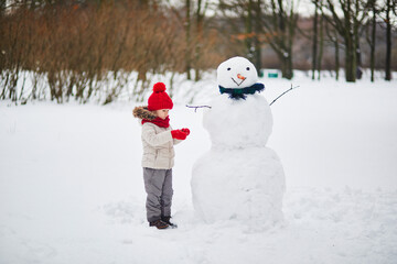 Adorable preschooler girl building a snowman on a day with heavy snowfall