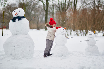 Adorable preschooler girl building a snowman on a day with heavy snowfall