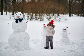 Adorable preschooler girl building a snowman on a day with heavy snowfall