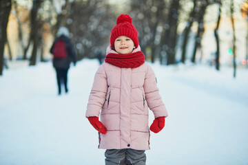 Adorable preschooler girl having fun in beautiful winter park on a snowy cold winter day