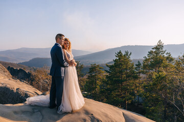 Incredible newlyweds standing on a rock against the background of an autumn forest