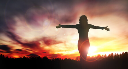 Happy standing woman looks at the sunset with open hands.