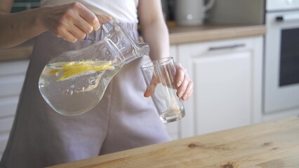 Beautiful slim woman drinks lemon water for detox. A young woman pours lemon water from a decanter...