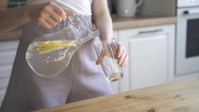 Beautiful slim woman drinks lemon water for detox. A young woman pours lemon water from a decanter and then drinks it.