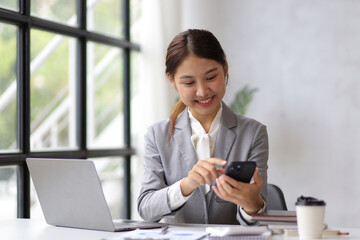 Attractive Asian woman in office using mobile phone texting and talking on smartphone.