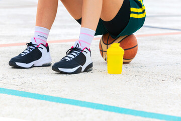 Close-up horizontal detail of the legs and shoes of a female basketball player sitting on a ball.