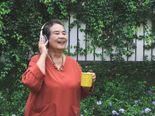  happy and healthy elderly asian woman   holding yellow  cup of coffee standing  in the garden,...
