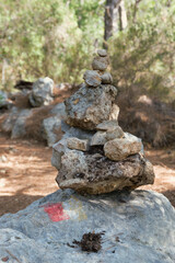 Trail Cairn in a forest indicating a trekking route for tourists. Marking the tourist route on the stones for navigation. Pile of stones used as hiking marker, next to a hiking trail sign