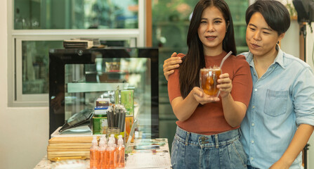 LGBT couple shows a cup of ice coffee to welcome other customers. Female girls take service from a coffee shop. Female partners enjoy ice drink with smiling faces. Two customers holding a cold drink.