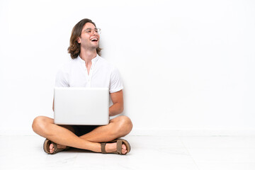 Young handsome man with a laptop sitting on the floor isolated on white background happy and smiling