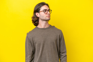 Caucasian handsome man isolated on yellow background looking to the side