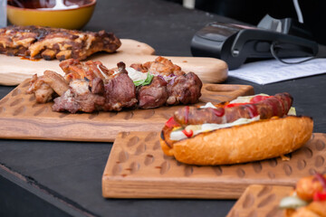 Sandwich, hot dog with sausage, beef ribs and shish kebab on wooden board on table at outdoor street food festival. Gastronomy and takeaway food concept