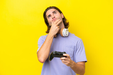 Young handsome caucasian man playing with a video game controller over isolated on yellow...