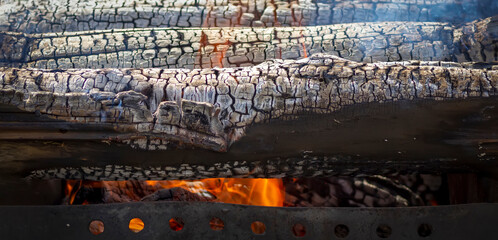 Large burning logs smoulder on the grill. Wood waste incineration