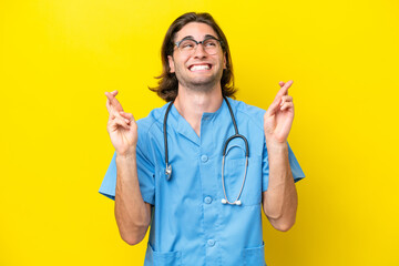 Young surgeon caucasian man isolated on yellow background with fingers crossing