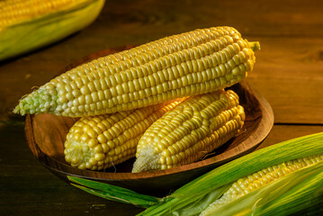 fresh raw organic ripe yellow uncooked sweet  corn cob dark rustic wooden table background closeup copy space agriculture  concept leaves plate autumn harvest banner. maize