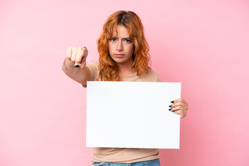 Young caucasian woman isolated on pink background holding an empty placard and pointing to the front