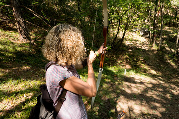 blond woman shooting with the bow in the forest