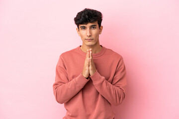 Young Argentinian man isolated on pink background keeps palm together. Person asks for something