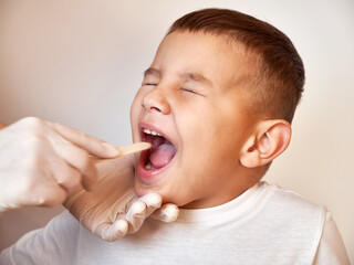 The doctor uses a spatula to examine the boy's throat.