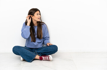 Young woman sitting on the floor listening to something by putting hand on the ear