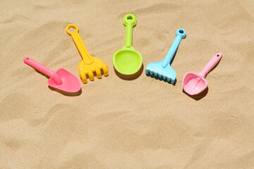 Fototapeta na wymiar Bright plastic rakes and shovels on sand, space for text. Beach toys