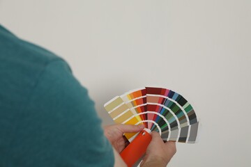 Man with palette choosing color for painting wall indoors, closeup. Interior design