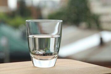 Glass of pure water on wooden table against blurred background, space for text