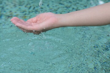 Water pouring into the girl's hand above pool, closeup