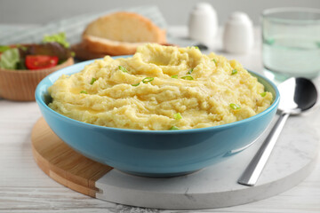 Bowl of tasty mashed potatoes with onion served on white wooden table, closeup