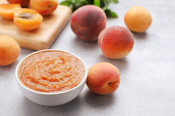 Apricot puree in bowl and fresh fruits on light grey table