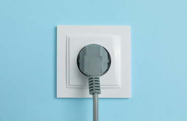 Power socket with inserted plug on light blue wall, closeup. Electrical supply