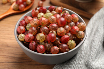 Obraz premium Bowl full of ripe gooseberries on wooden table, closeup