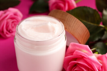 Glass jar of face cream and roses on pink background, closeup