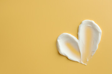 Samples of face cream in shape of heart on yellow background, top view. Space for text