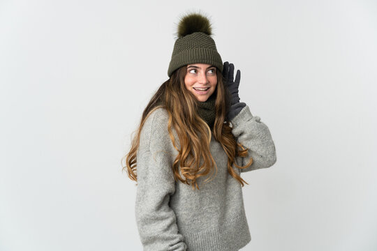 Young caucasian woman with winter hat isolated on white background listening to something by putting hand on the ear