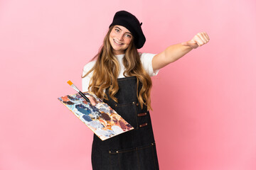 Young artist woman holding a palette isolated on pink background giving a thumbs up gesture