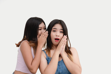 A teenage girl is shocked to hear about the recent issue from her best friend, who is whispering to her. Two talkative pals gossiping about a rumor. Studio shot isolated on a white background.