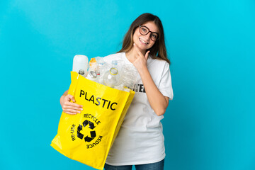 Woman holding a bag full of bottles to recycle isolated on blue background happy and smiling