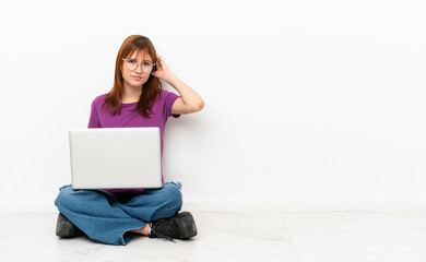 Fototapeta premium redhead girl with a laptop sitting on the floor having doubts