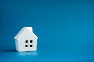 A simple miniature ceramic white house model on blue background with copy space, minimal style. Concepts of residential or real estate property, land and building business and family life.
