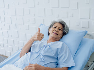 Happy Asian senior woman patient grey hair smiling, thumb up and looking at camera while lying on...