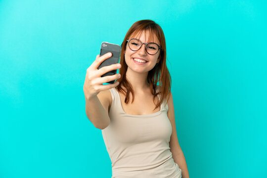 Redhead girl isolated on blue background making a selfie