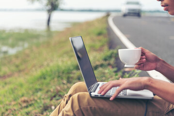 Man hands typing laptop notebook holding coffee cup outside office. Close up man hands using computer laptop sit on green park outdoors lifestyle. freelancer Men using laptop home office technology